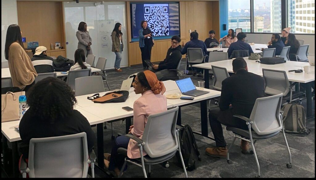 A photo taken of students spread out across a classroom listening to a presentation from one of the teams