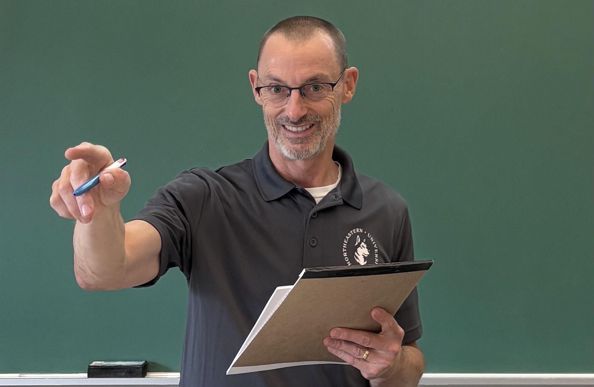 Professor Sean Cumming in a portrait photo, standing in a classroom and gesturing while smiling